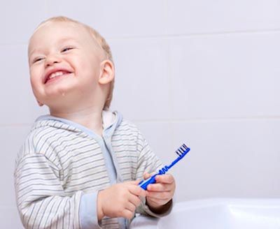 toddler smiling while brushing his teeth