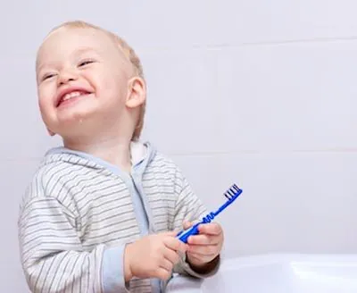 toddler smiling while brushing his teeth